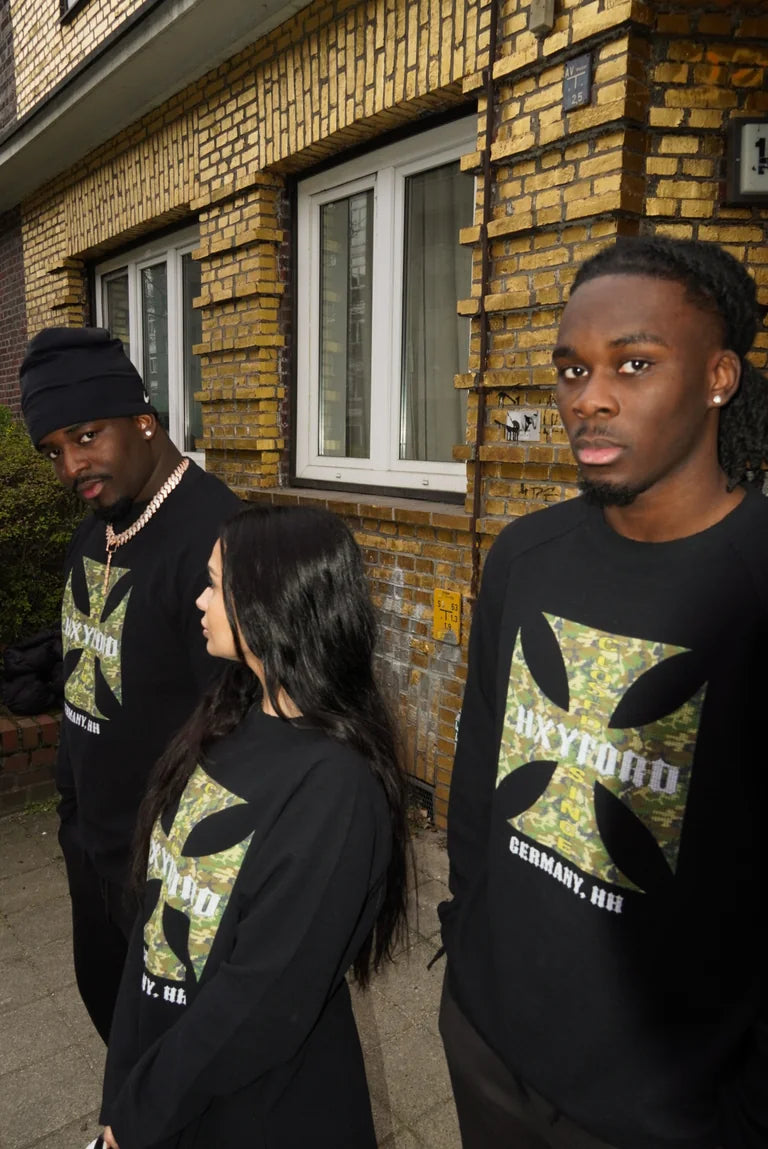 Drei Models in schwarzen HXYFORD-Sweatshirts vor einer Backsteinfassade.