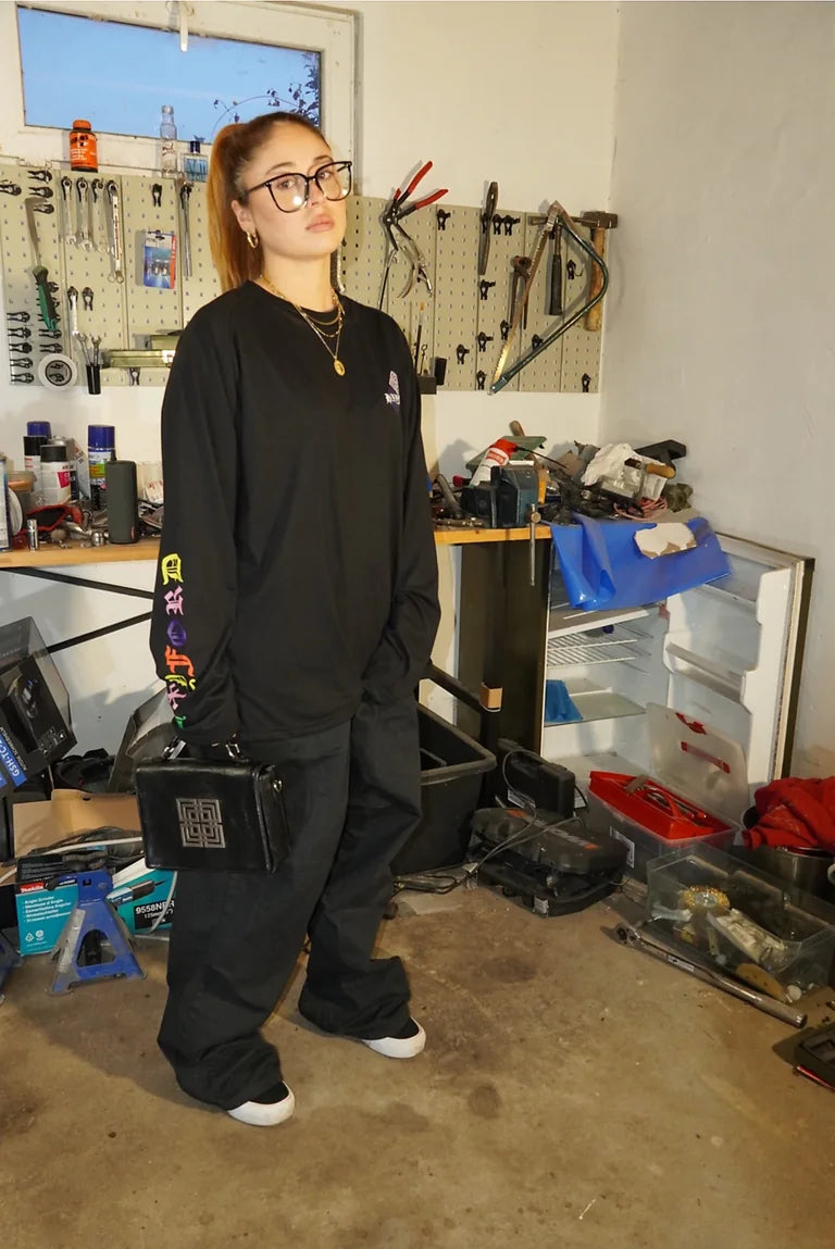 Model im schwarzen HXYFORD-Longsleeve mit buntem Ärmelprint und schwarzer Tasche.