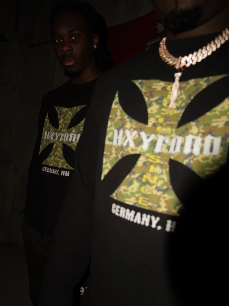 Detail des grün gemusterten HXYFORD-Grafikprints auf einem schwarzen Sweatshirt.